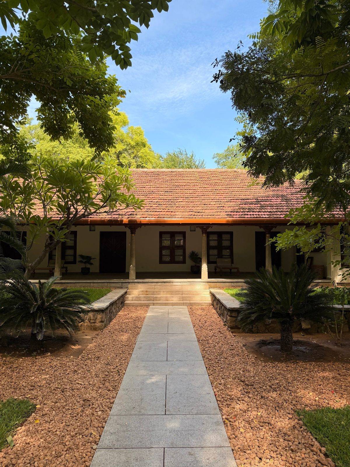 Traditional Indian farmhouse with terracotta tiled roof, stone verandah columns and a garden pathway