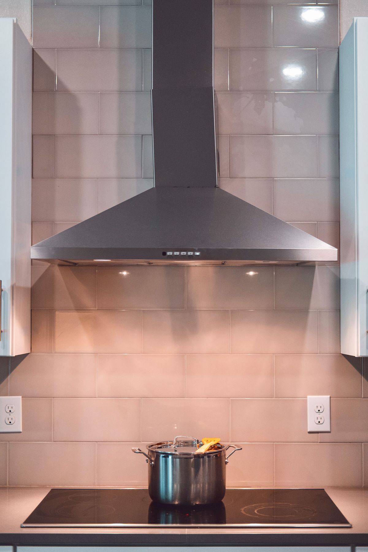 Stainless steel pyramid chimney mounted above a glass cooktop in a modern kitchen